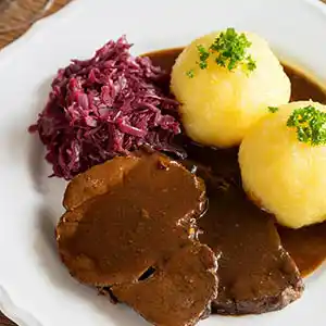 Teller mit Schweinebraten, Knödel und Krautsalat an Biersauce.