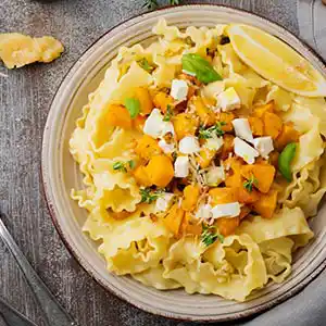 Teller mit Nudeln, gebratenem Kürbis und Fetakäse.