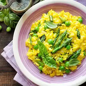 Teller mit Risotto, Safran, Erbsen und Spargel.