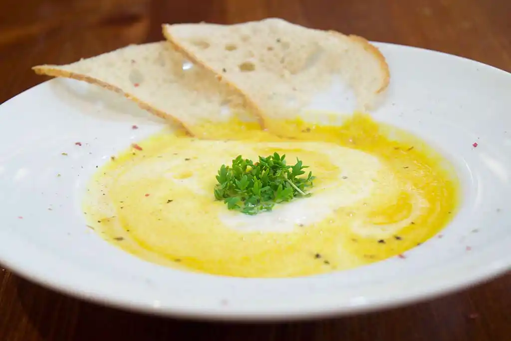Auf Teller angerichtet Kürbiscremesuppe mit geröstetem Weißbrot.