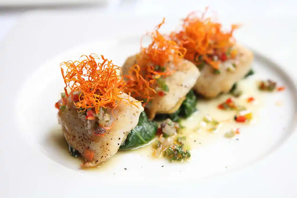 Auf Teller angerichtet Seehecht auf Spinatnestern und Karotten an Buttersauce.