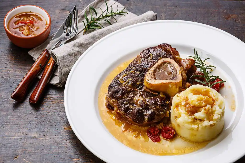 Teller mit Ossobuco. Kalbsbeinscheiben mit Kartoffelstampf an Bratensauce.