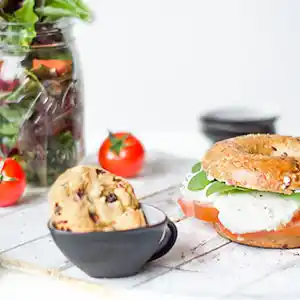 Holzbrett mit Bagel, Tomaten und Mozzarella, gemischter Salat und Cookie.