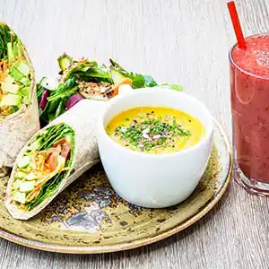 Holzbrett mit Wraps, Gemüsefüllung und Käsedip, Salat mit Kernen und Smoothie.
