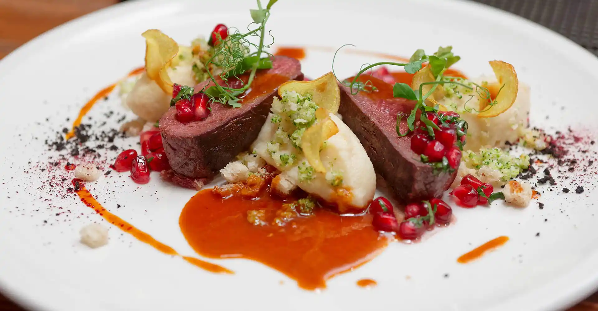 Teller mit rosa gebratenem Rinderfilet an Kohlrabipüree, Kartoffelchips und Cranberries.