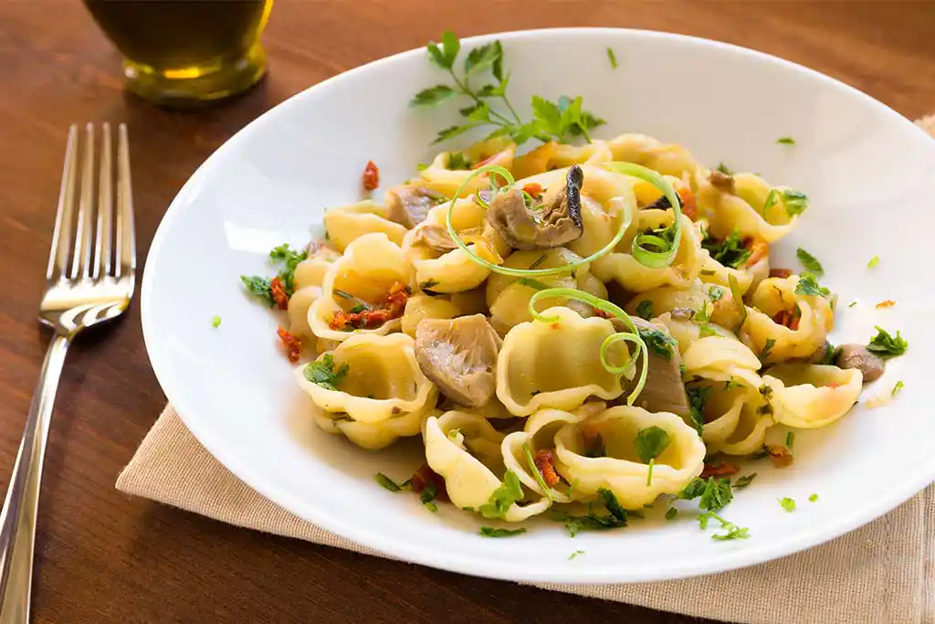 Teller mit Nudeln, Zucchini, Pilzen und Kapern.