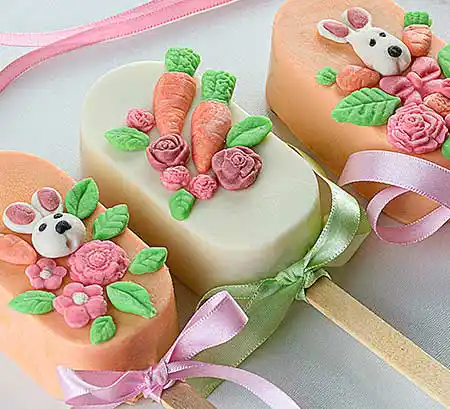 Bunte Cakesicles mit Deko aus essbaren kleinen Karotten und anderen Motiven.