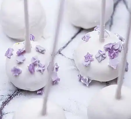 Weiße Cake-Pops auf Marmorplatte mit Topping aus Mini-Marzipan-Blüten.