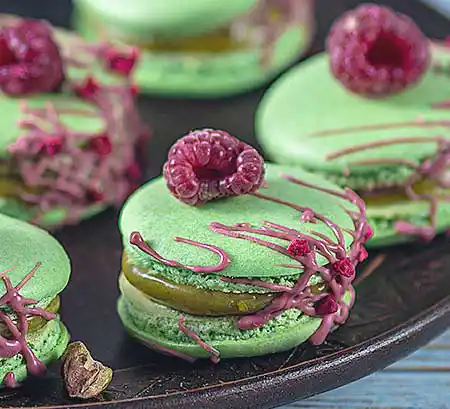 Teller mit grünen Macarons und Himbeeren.