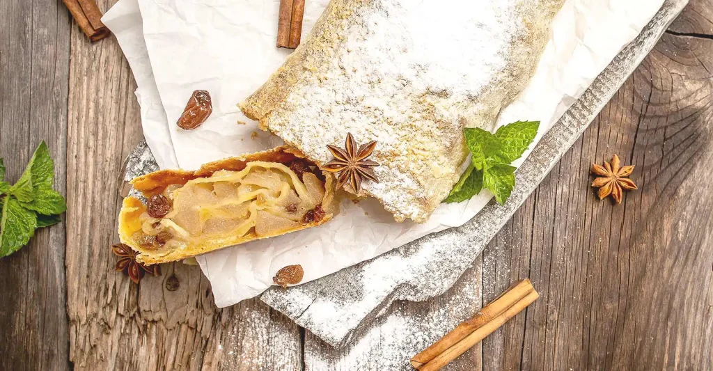 Holtisch mit angeschnittenem Apfelstrudel auf Backpapier mit Sternanis.