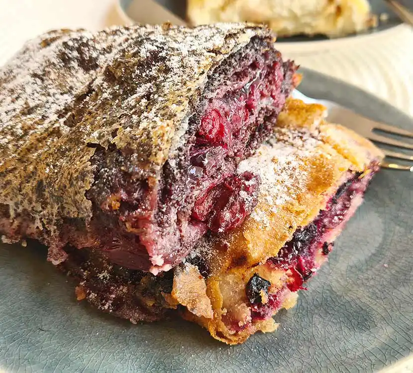 Zwei große Stück Rote-Beeren-Mohnstrudel auf Teller.