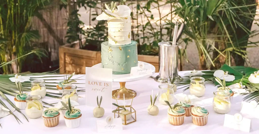 Gedeckter Tisch mit Hochzeitstorte, Cupcakes und Cakepops auf Tellern angerichtet mit Blumendekor.