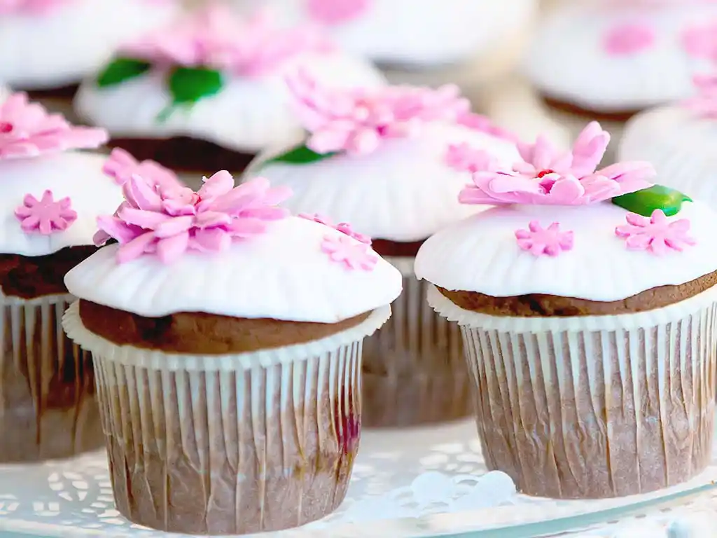 Tablett mit Cupcakes, weißem Topping und rosa Blüten.