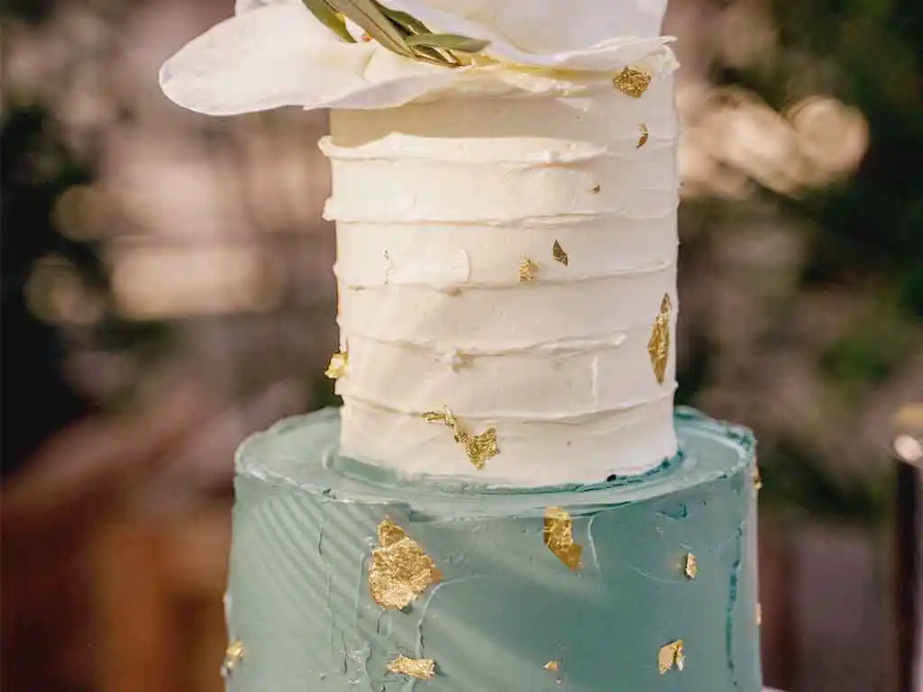 Grün-weiße Hochzeitstorte mit Goldapllikationen und weißen Blüten.