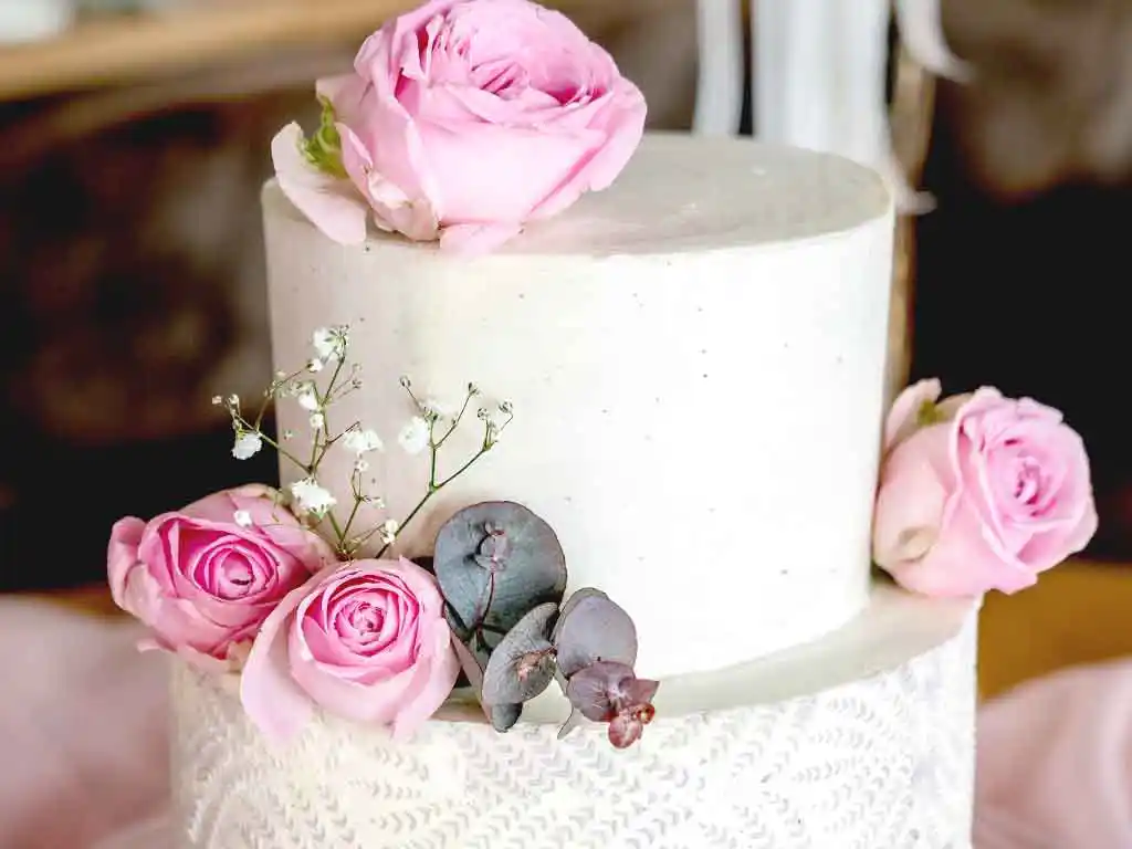 Tisch mit 2-stöckiger weißer Hochzeitstorte mit Rosen-Blumendekor.