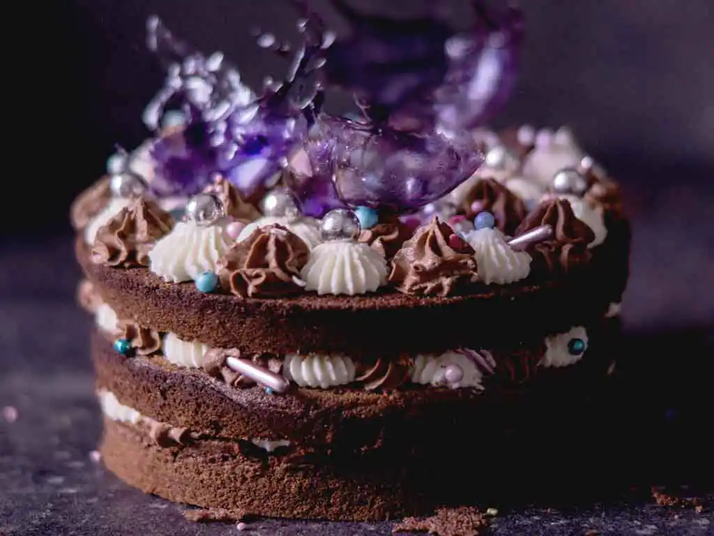 Dunkle Schokotorte mit weißen Applikationen und violetten Blumen.